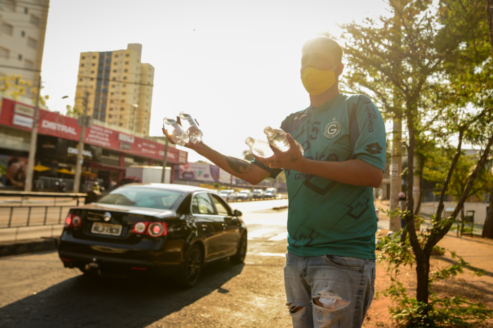 Imagem colorida mostra um homem usando uma camiseta verde e uma calça jeans. Ele está na calçada, debaixo de um sol forte.