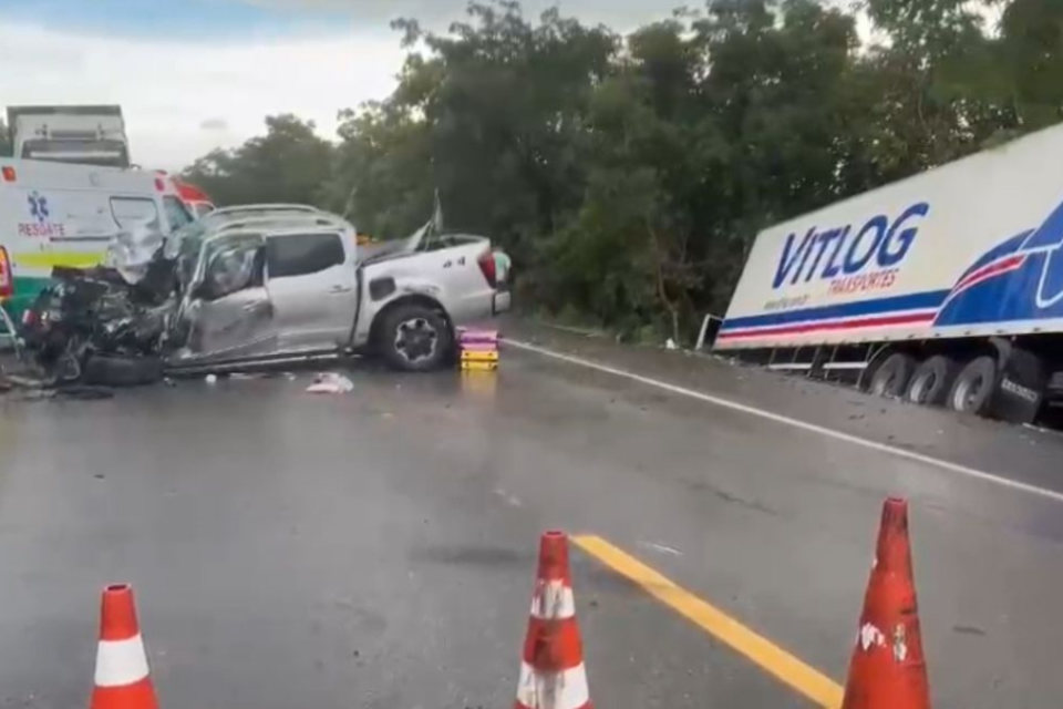 Imagem colorida mostra uma caminhonete com a frente completamente destruída após bater em um caminhão que está do outro lado da via.