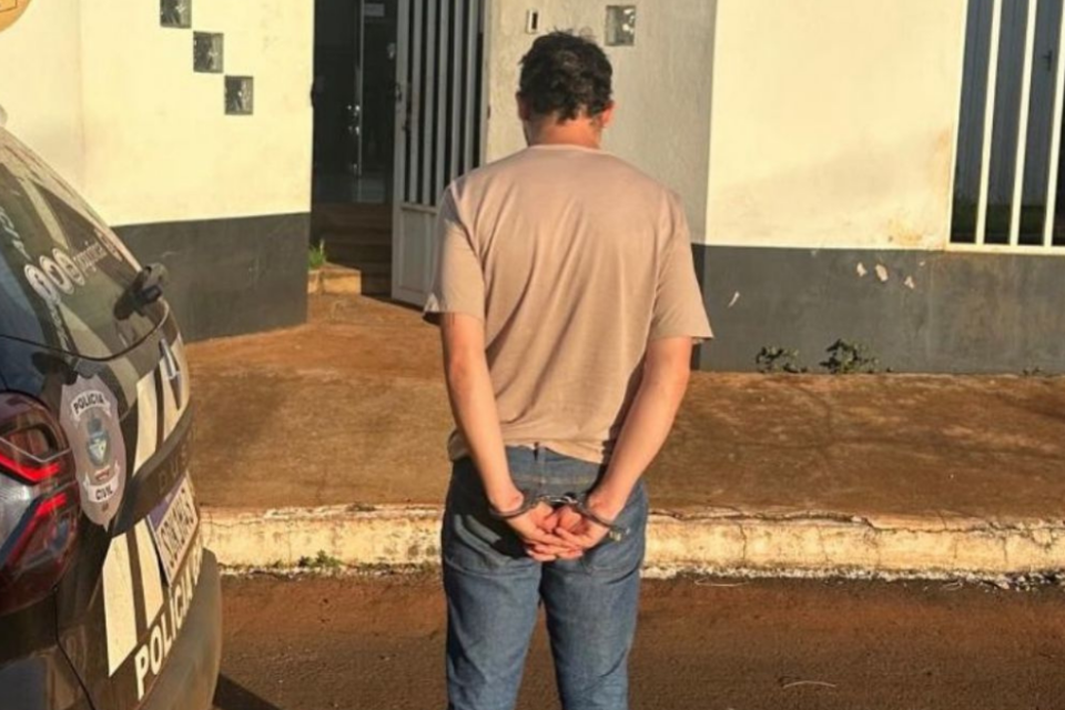 Imagem colorida mostra um homem virado de costas com as mãos para trás. Ele usa uma camiseta clara e uma calça jeans.