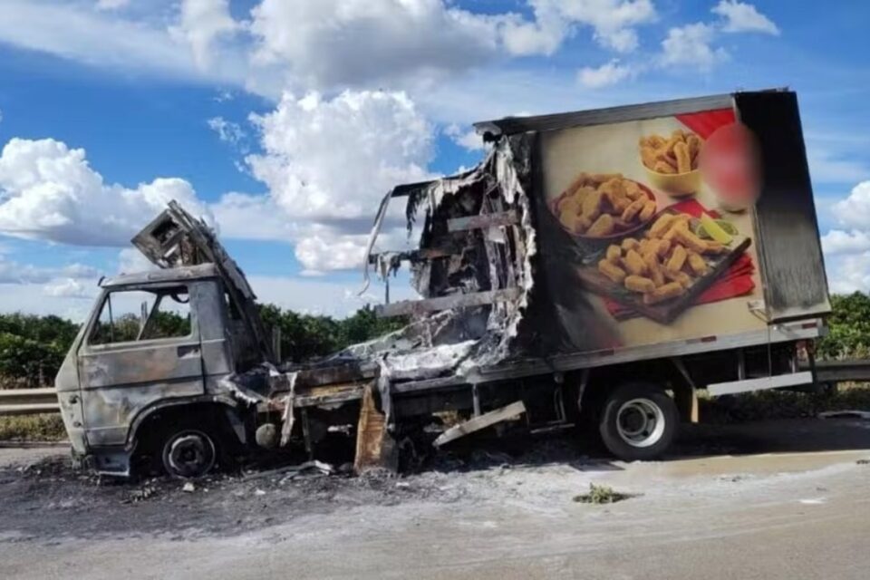 A imagem mostra um caminhão baú parcialmente destruído