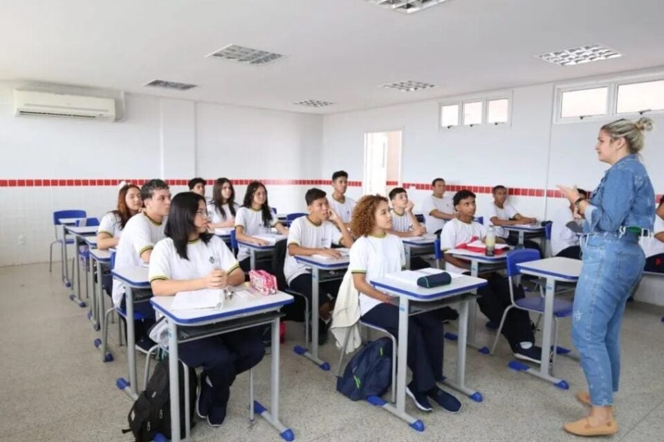 A imagem mostra uma professora dando aulas para alunos