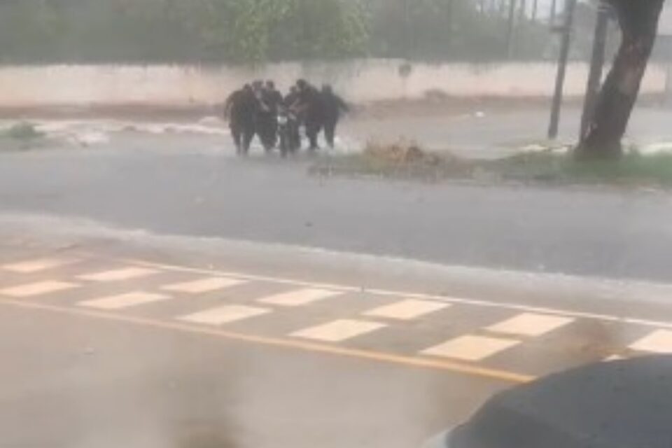 A imagem mostra uma equipe da Rotam resgatando um motociclista preso na enxurrada