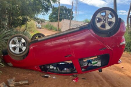Imagem colorida mostra um carro vermelho de cabeça para baixo após bater em uma árvore.