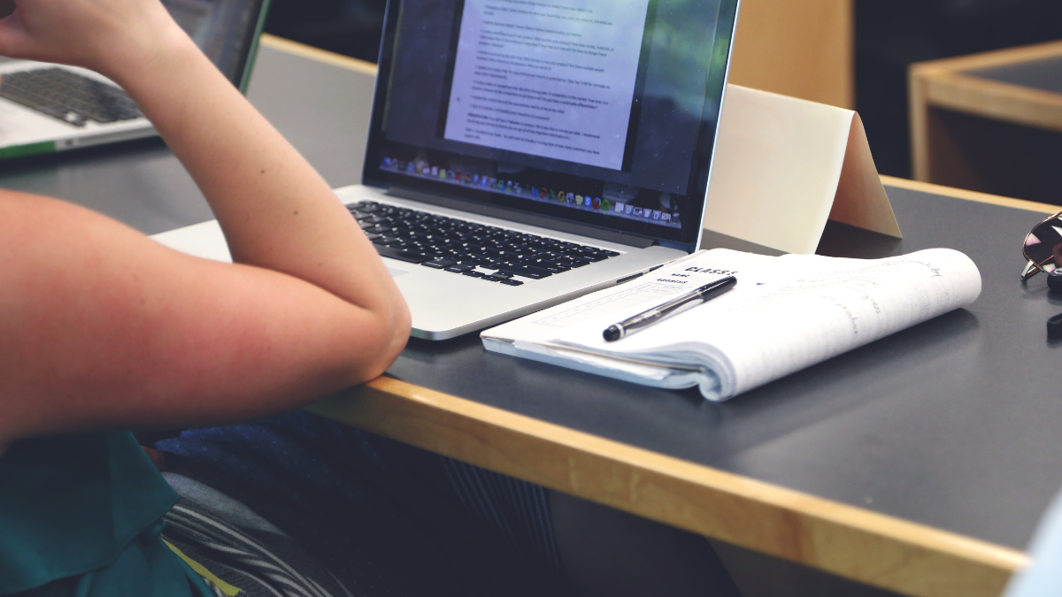 Imagem de uma pessoa estudando com um notebook e um caderno na mesa