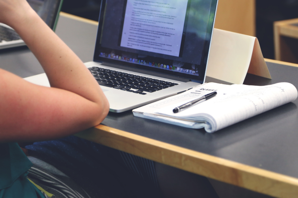 Imagem de uma pessoa estudando com um notebook e um caderno na mesa