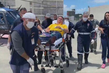 Foto colorida mostra Bolsonaro em uma maca sendo levado para atendimento hospitalar