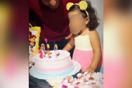 A imagem mostra a menina apagando as velinhas do bolo