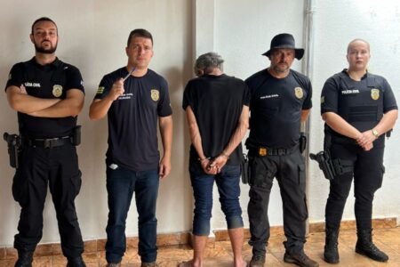 Imagem do homem preso ao lado do delegado e policiais