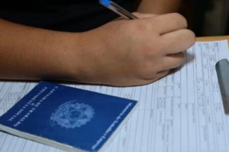 Imagem de alguém preenchendo uma prancheta, com a carteira de trabalho ao lado