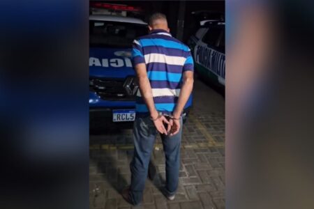 Imagem do homem preso de costas para a câmera e algemado