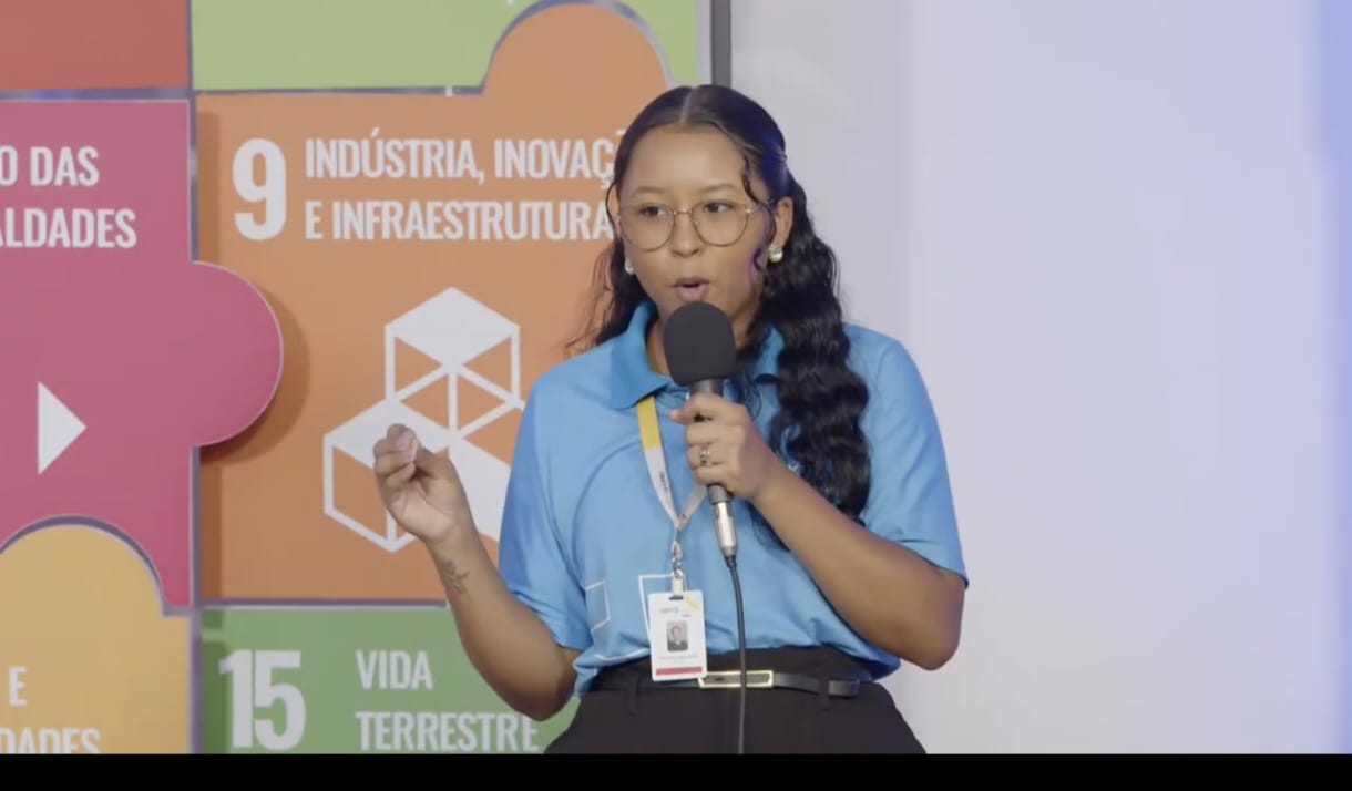 Mulher jovem de cabelos longos ministra palestra e segura um microfone na mão