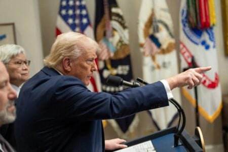 Trump aponta com o dedo com bandeira dos EUA ao fundo