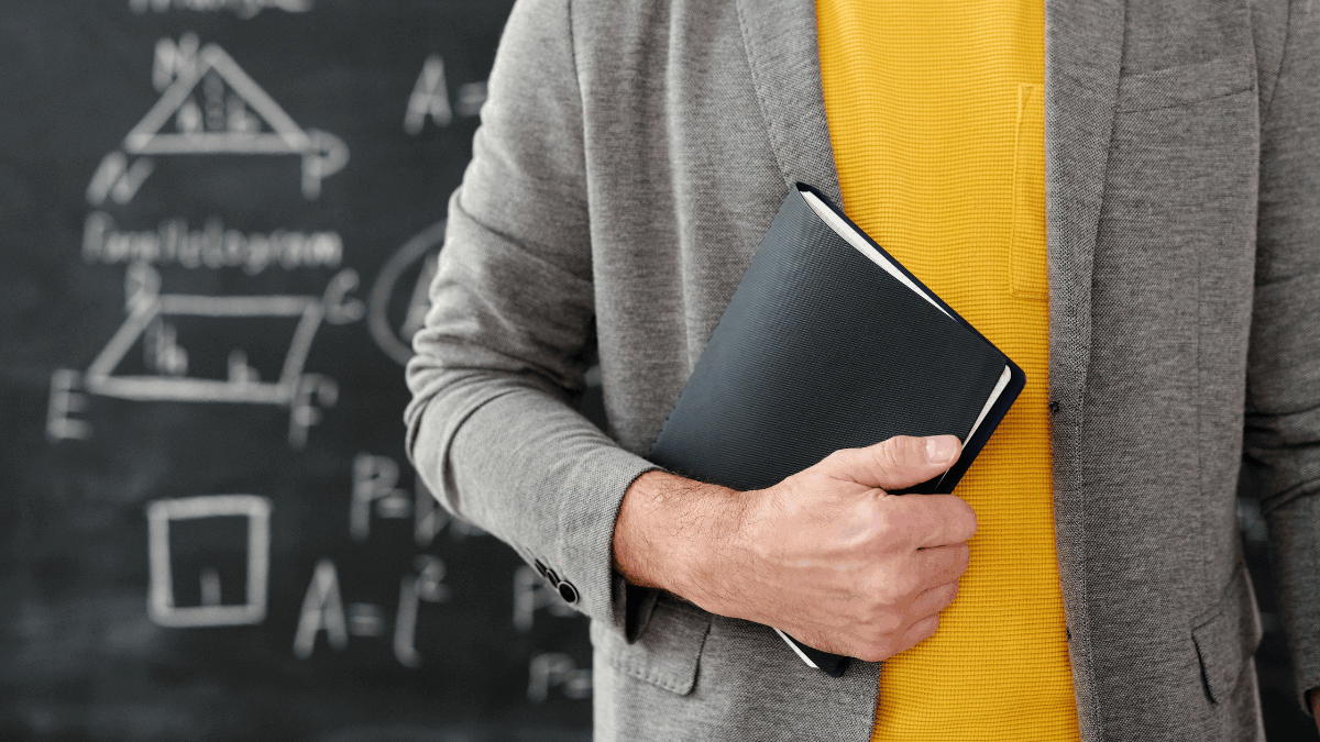 Imagem de um professor de exatas segurando um livro