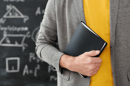 Imagem de um professor de exatas segurando um livro