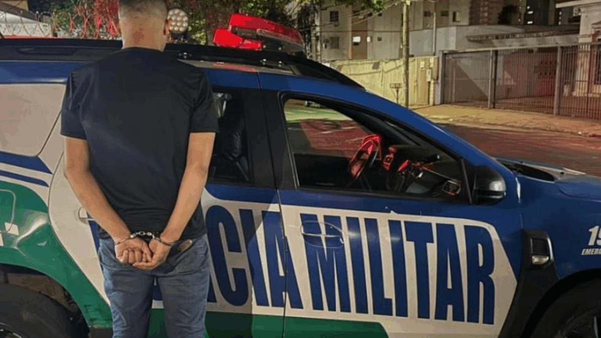 Homem algemado de costas próximo a um carro da Polícia Militar