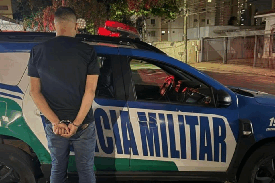 Homem algemado de costas próximo a um carro da Polícia Militar