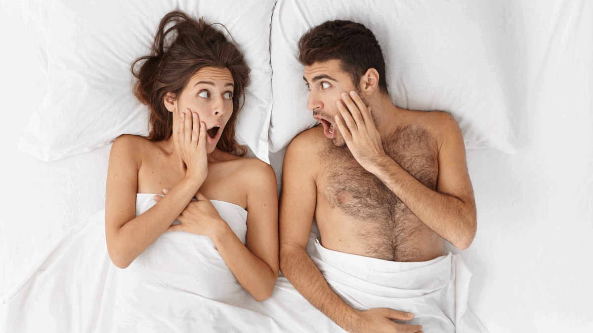 Mulher e homem deitados em uma cama com lençóis brancos e com expressão surpresa