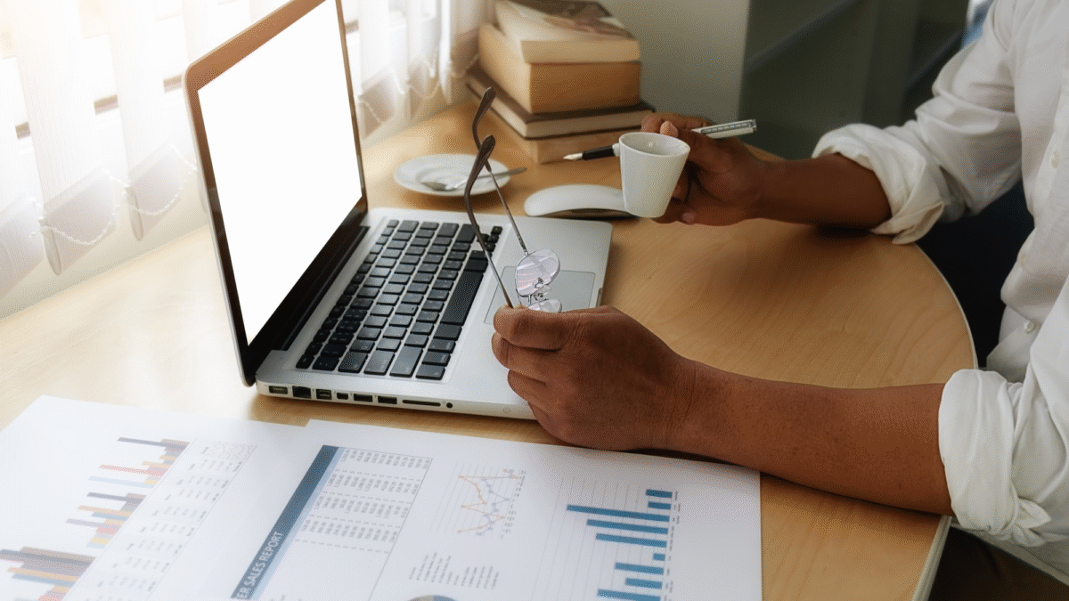 Mãos de homem sobre o teclado de um notebook em uma mesa cheia de papéis