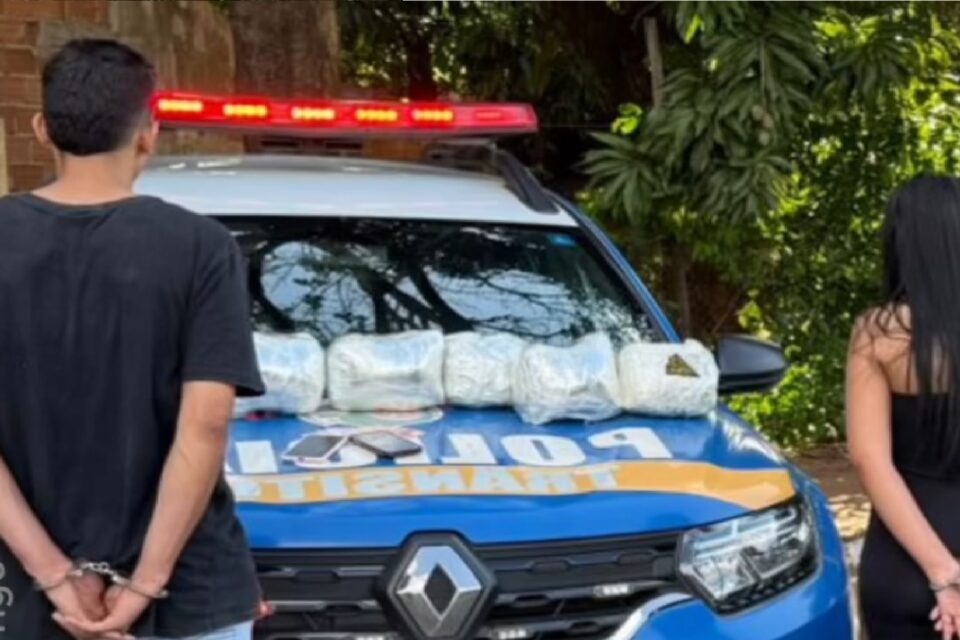 Imagem mostra casal preso e posicionado em frente a viatura da Polícia Militar de Goiás