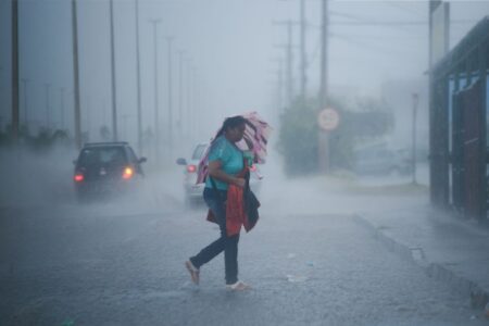 Imagem mostra mulher atravessando rua em meio a chuva forte