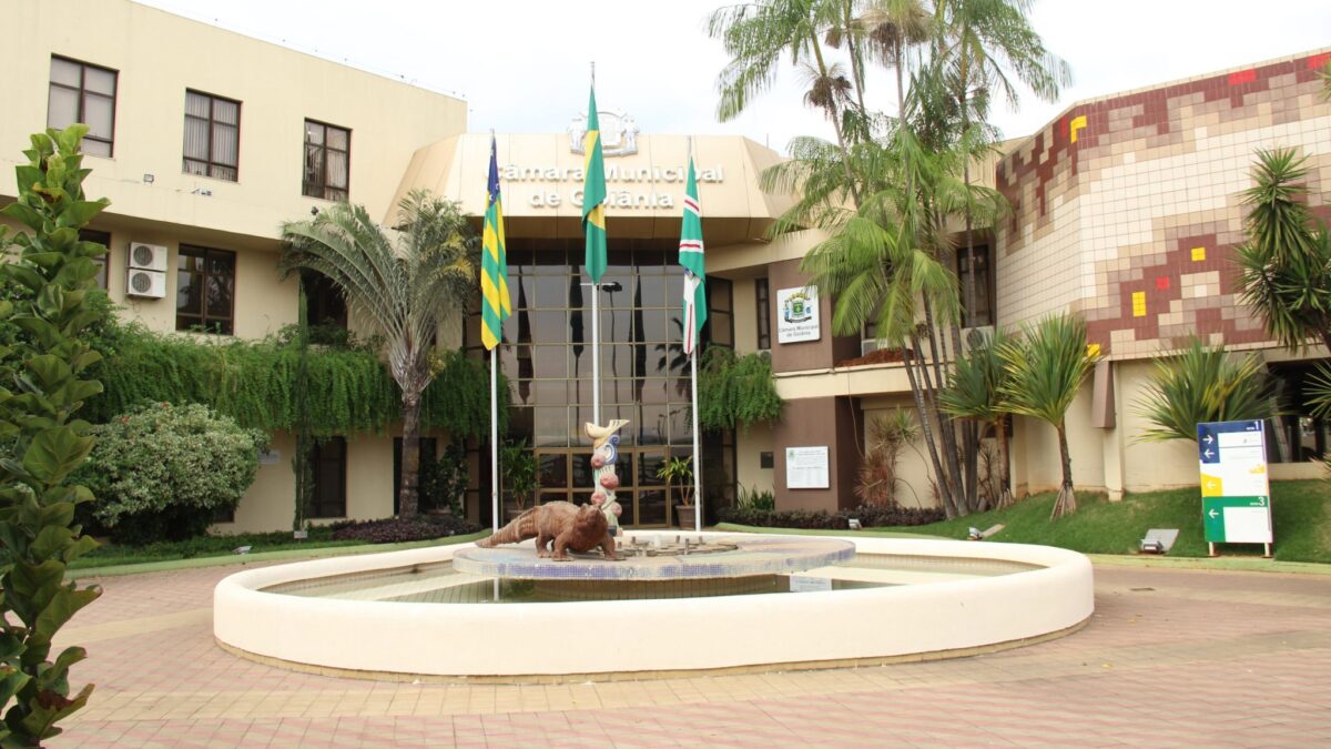 Imagem mostra entrada principal do prédio da Câmara Municipal de Goiânia. Ao fundo, bandeiras de Goiânia, Goiás e do Brasil