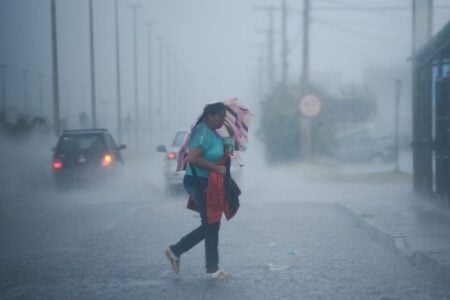 Imagem mostra mulher transitando sob forte chuva