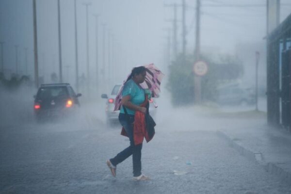 Imagem mostra mulher transitando sob forte chuva