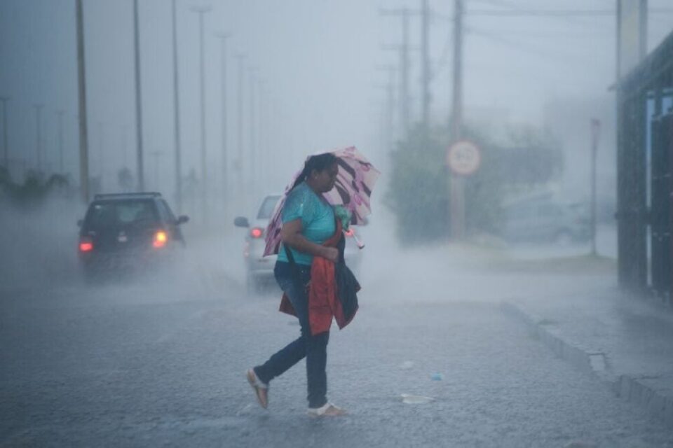 Imagem mostra mulher transitando sob forte chuva
