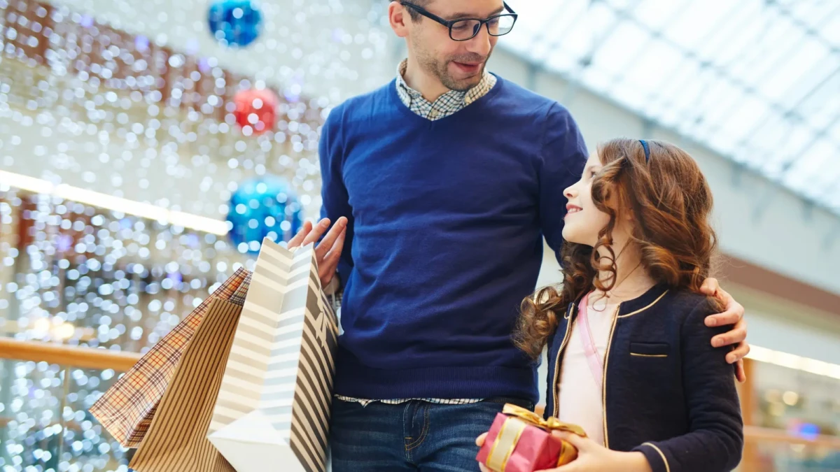 Pai e filha passeiam no corredor de shopping com sacolas nas mãos