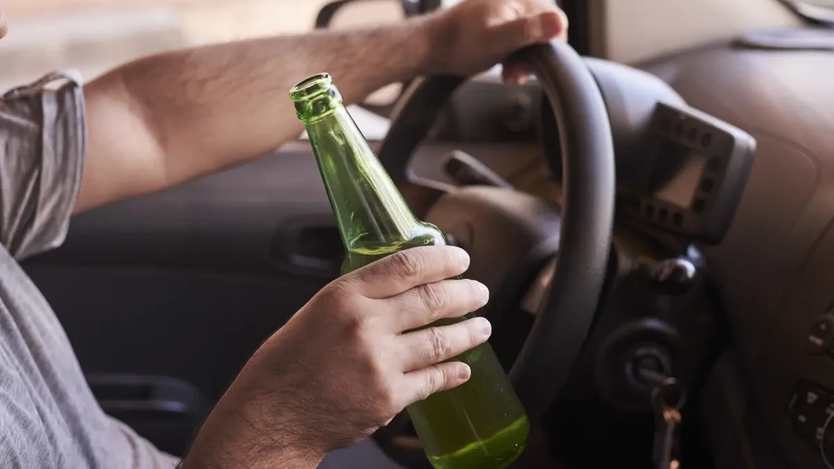 Imagem de um homem segurando uma garrafa de bebida enquanto dirige