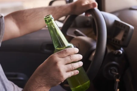Imagem de um homem segurando uma garrafa de bebida enquanto dirige
