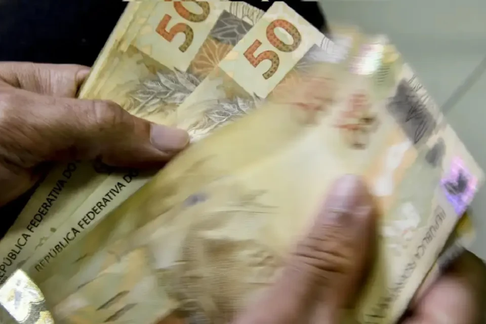 Imagem mostra pessoa segurando várias notas de R$ 50,00