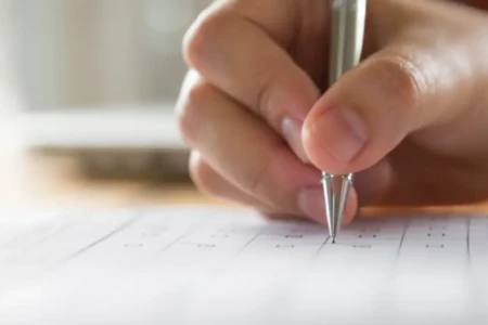 Imagem e uma pessoa preenchendo o gabarito de uma prova