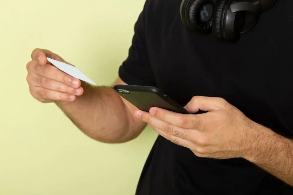 jovem-homem-de-camiseta-preta-segurando-um-cartao-branco-e-usando-um-telefone-verde