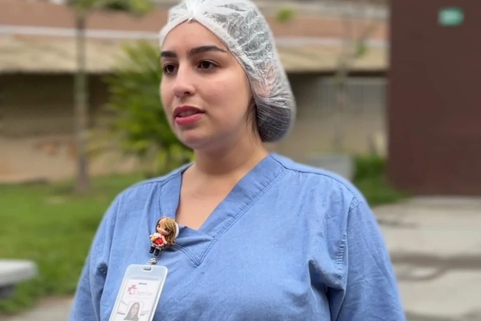 Enfermeira em plano americano com jaleco azul, touca branca e crachá