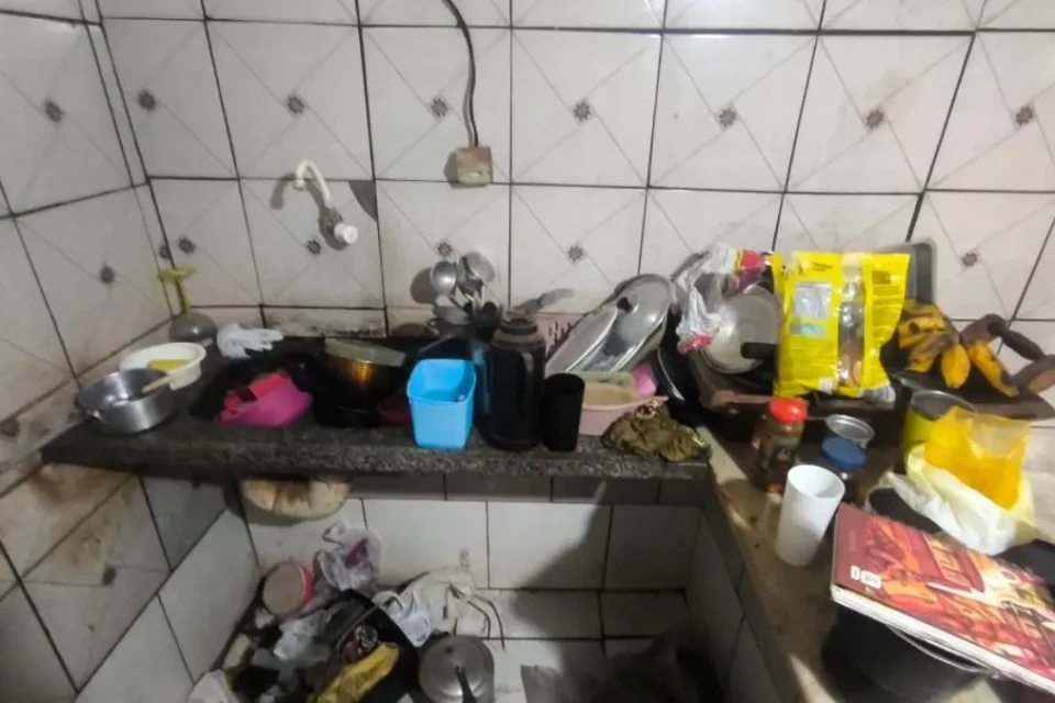 Cozinha com louças na pia, alimentos e louças espalhados e sujos.