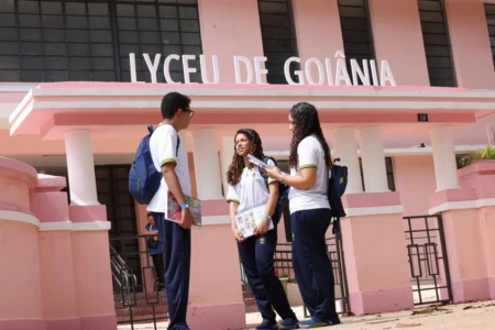 Estudantes em frente à entrada do colégio Lyceu de Goiânia. Eles vestem uniformes