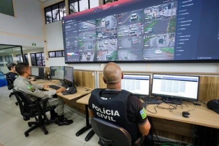Policiais em frente a um centro de comando com telas e computadores
