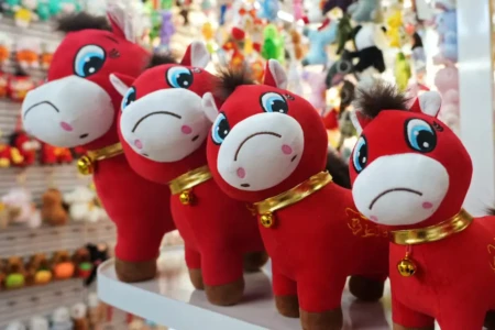 Quatro cavalos de pelúcia com expressão triste. Eles são vermelhos e têm um colar dourado com um sino.