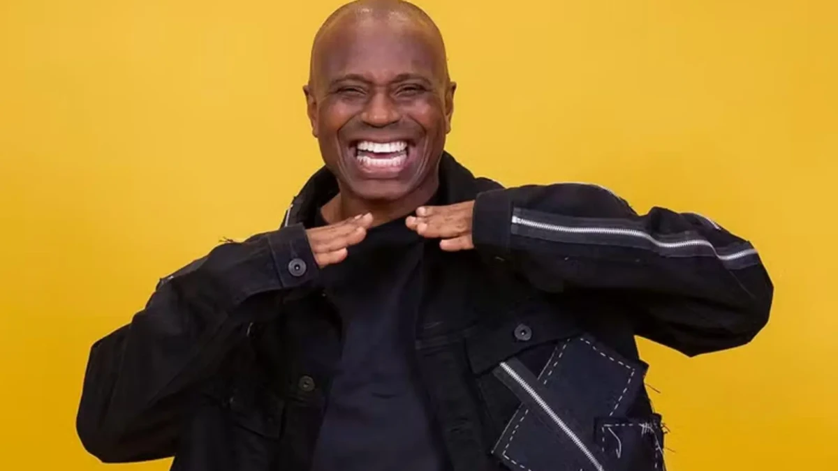 Homem negro sorri. Ele veste um casaco escuro e é careca