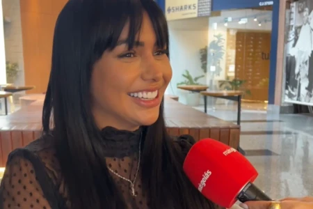 Mulher sendo entrevistada. Ela tem cabelos longos, escuros e está sorrindo.