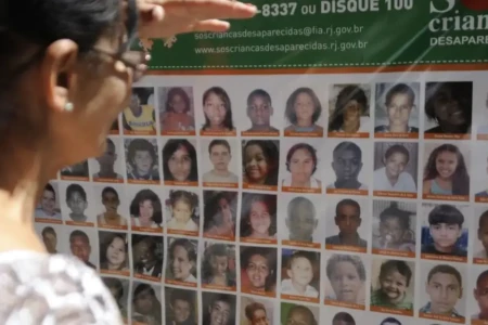 Imagem mostra mulher consultando placa com fotos de crianças desaparecidas