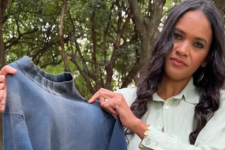 Uma mulher de cabelos longos e roupa clara segura uma blusa de frio azul desgastada.