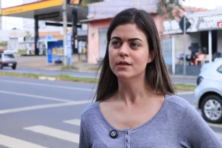 Mulher de cabelos longos e escuros e blusa cinza é entrevistada na rua