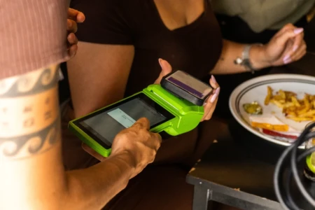 Garçon segura a máquina de pagamento de cartão e oferece ao cliente que está sentado