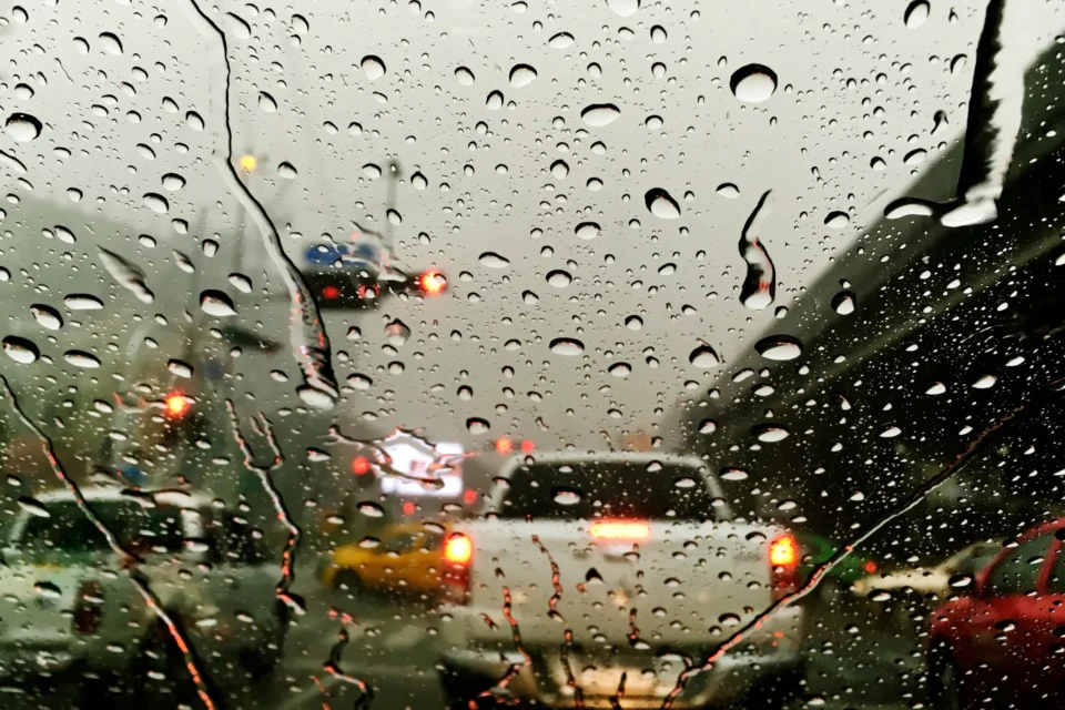 Imagem de veículos sendo visto através de um vidro com marcadas de água de chuva