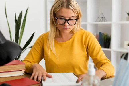 Mulher de cabelos loiros e óculos sentada em uma mesa estudando