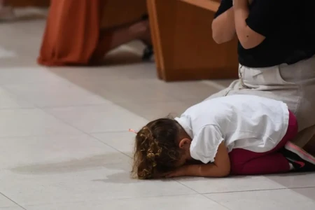 Imagem mostra criança acompanhada da mãe durante missa