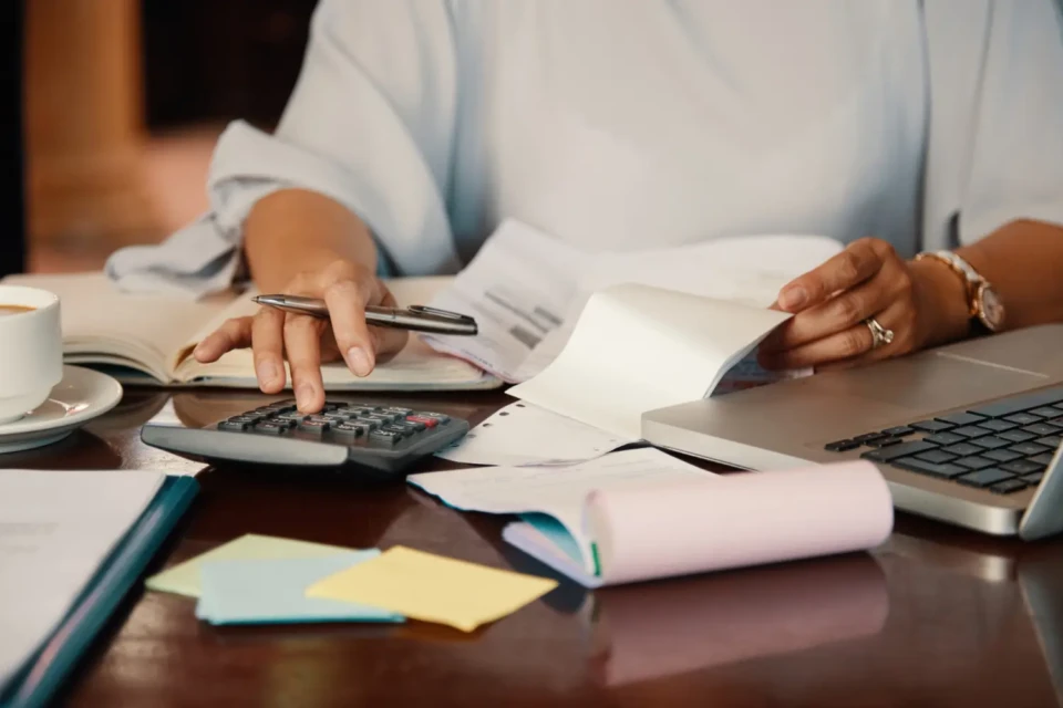 Mão feminina fazendo cálculo na calculadora em meio a papéis sobre a mesa