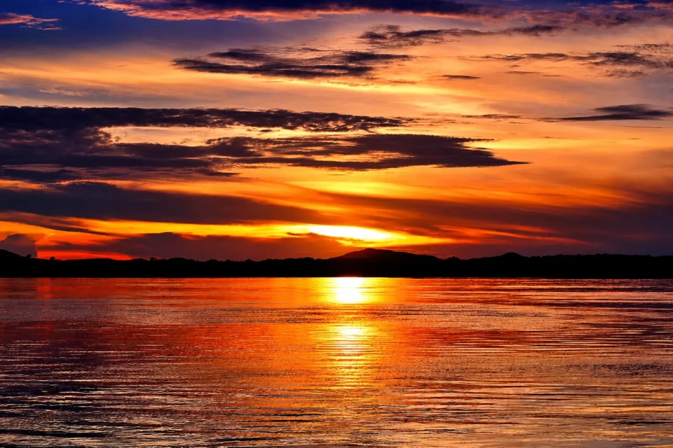 Pôr do sol no Rio Araguaia colore o céu com tons alaranjados durante a temporada de julho, um dos períodos de maior movimento turístico em Goiás e que reúne milhares de famílias às margens do rio. Crédito da foto: Arquivo / Goiás Turismo.
